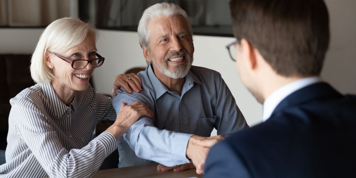 Senior couple smiling and shaking hands with a real estate advisor