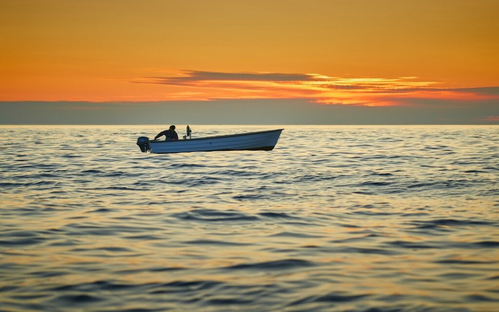 Professional deep sea fishing boat on the open ocean with the sun rising on the horizon, symbolizing a new day of opportun...