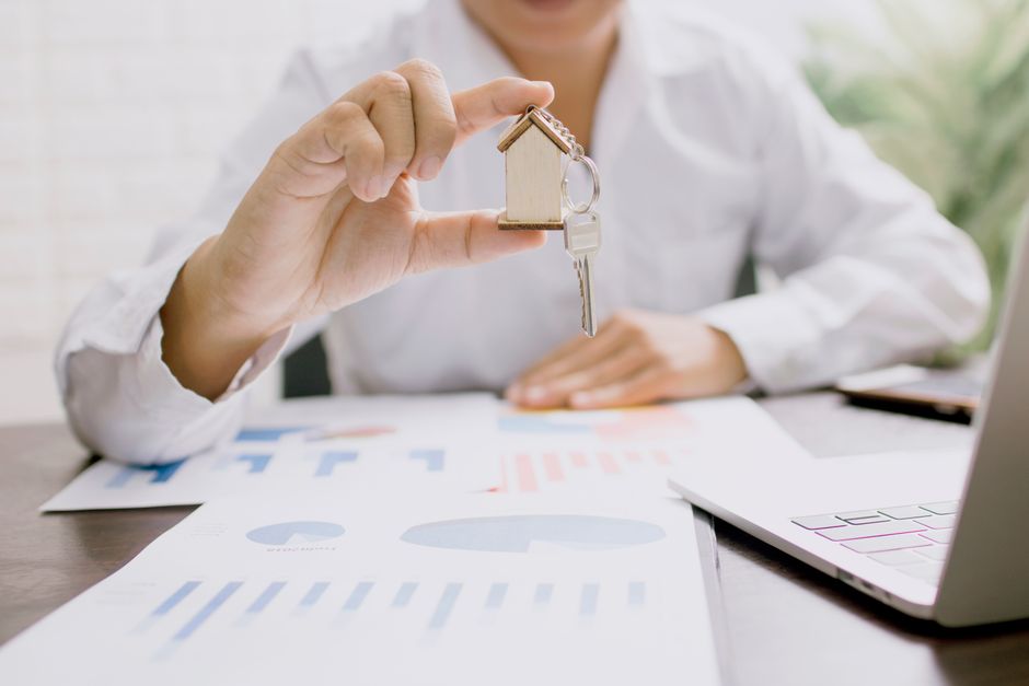 Close-up of a hand holding a set of house keys with the blurred background of a modern home, representing a successful property sale.