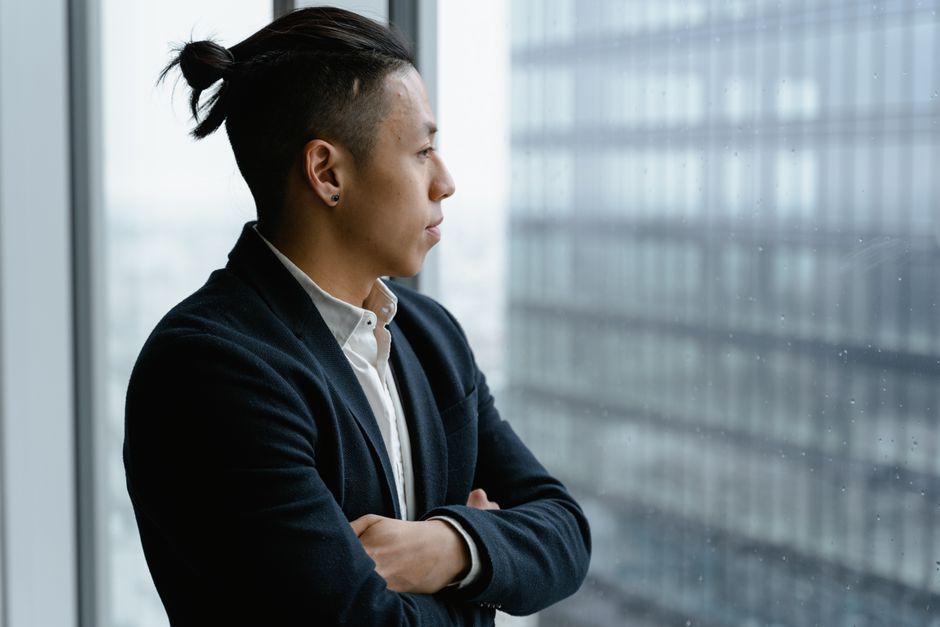 A professional entrepreneur stands in a high-rise office, looking out a large window at a sprawling cityscape, contemplating their choice of real estate franchise.