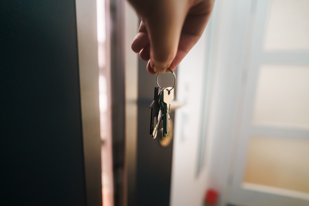 Professional solo real estate agent stands confidently in front of a modern home, holding up a single house key symbolizin...